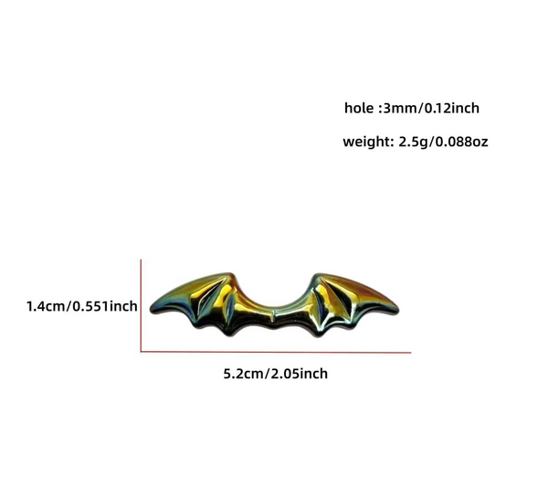 A small bat-wing shaped accessory or charm is shown on a plain white background with printed dimensions and weight information above it. The product appears glossy and iridescent, shifting between gold, green, and dark tones.